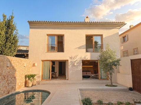Rear exterior of Can Bella, a luxury new-build townhouse in Muro, Mallorca, featuring a private courtyard, swimming pool, olive tree and timber-framed doors.
