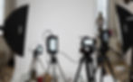 Cameras on tripods with studio lighting equipment in front of white backdrop.