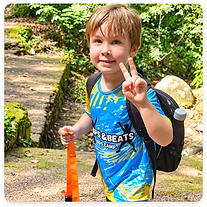 A child in a blue Leaps & Beats shirt poses outdoors among greenery.