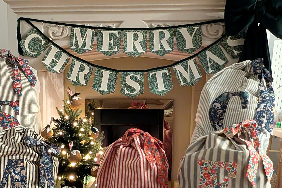 Christmas scene with striped gift bags by a small lit tree. "Merry Christmas" banner hangs above a fireplace, creating a festive mood.