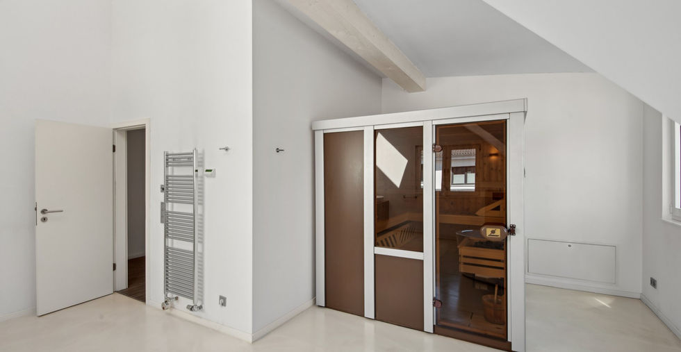 Modernes Tageslichtbadezimmer mit integrierter Sauna, verchromtem Heizkörper, sichtbarem Deckenbalken unter geöffneter Decke im großen Einfamilienhaus in Langenfeld.