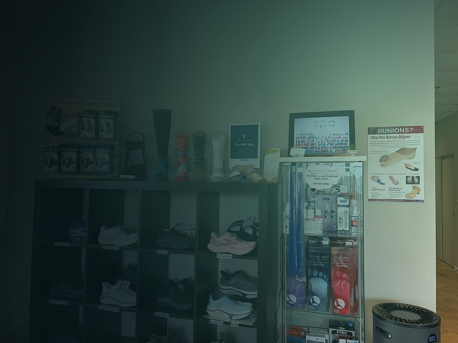 Interior of Parkway Back and Foot Clinic in Stoney Creek with shelves of footwear, a cabinet of medical therapy products and posters of foot care, services and clinic information on the wall.