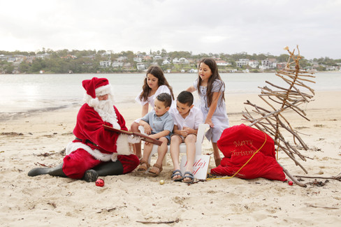 Santa reading Christmas story to two girls and two boys on the beach