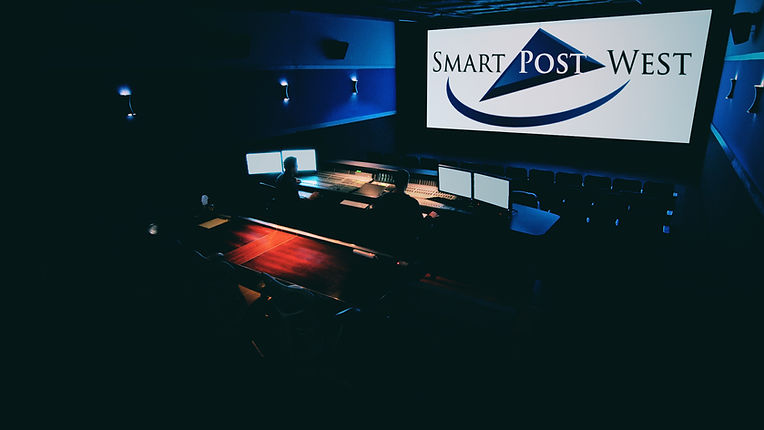 Theatrical mixing stage at Smart Post West featuring a large Christie projector, Dolby surround, an Avid mixing console, and tiered seating designed for immersive theatrical audio post-production. A silhouetted re-recording mixer sits at the console mixing a feature film.