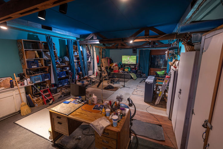 Reverse angle of the Foley stage at Smart Post Sound Burbank, California, showing a large wooden desk, organized shelves with props and tools, and a recording zone with microphones and textured surfaces for Foley performance.