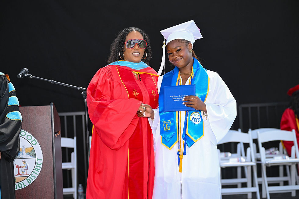 A graduate holding a diploma poses with a school official in red academic robes beside the Inglewood Unified podium