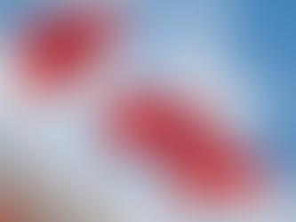 Three red flags waving on tall poles against a blue sky with clouds. The setting has a building corner in the foreground.