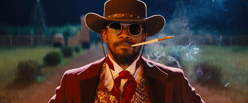 Homem está olhando em direção à câmera com um cigarro na boca e trajando chapéu, óculos escuros e uma roupa elegante. Está à noite e é possível ver a fumaça do charuto.