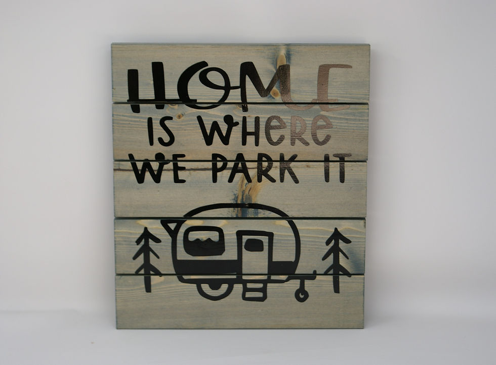 Worn navy wood plank sign with Home is where your Park it written on it along with RV camper in the woods.