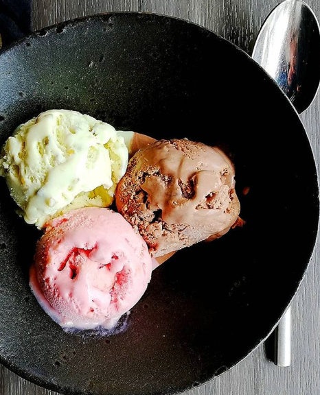 A scoop of vanilla, a scoop of chocolate, and a scopp of strawberry ice cream form a triangle in a bowl.