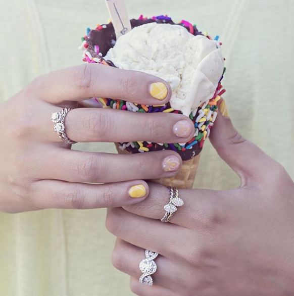 A woman wearing rings holds a waffle cone dipped in chocolate and sprinkles filled with vanilla ice cream.