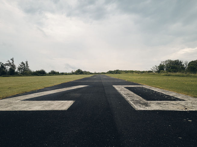 geteerte Startbahn eines Segelflugplatzes mit weißer Beschriftung in trüber Wolkenstimmung