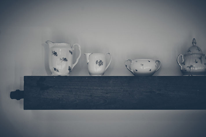 Stillleben mit alten Kaffeekännchen, stehend auf einer quer an der Wand angebrachten Orgelpfeife aus Holz in schwarzweiß