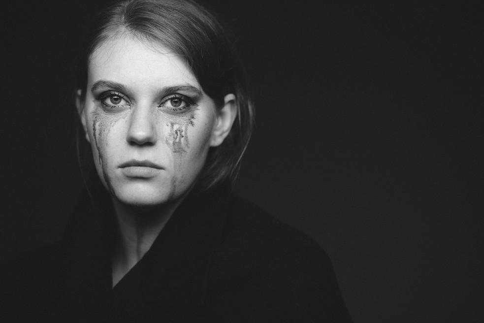 Close Up Portrait einer jungen Frau mit einer durch Tränen stark verschmierten Schminke vor dunklem Hintergrund