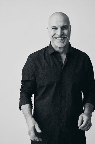 Schwarzweiß Portrait eines tanzenden und lachenden Mannes im dunklen Hemd vor hellem Hintergrund