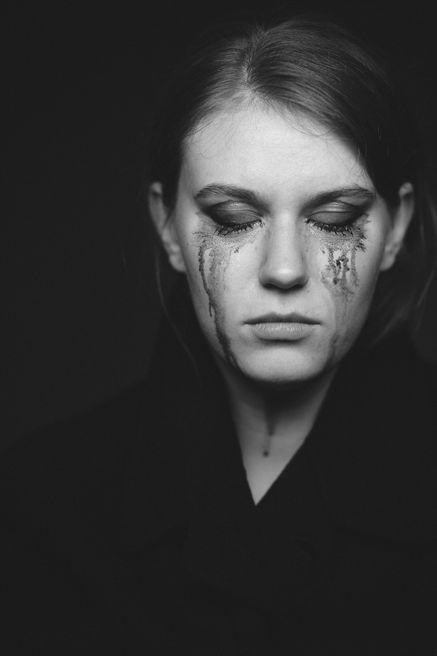 Close Up Portrait einer jungen Frau mit geschlossenen Augen und einer durch Tränen stark verschmierten Schminke vor dunklem Hintergrund