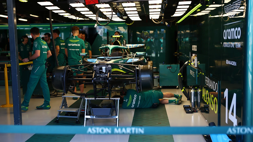 Vista del interior del garaje de Aston Martin con mecánicos trabajando bajo el coche de Fernando Alonso.