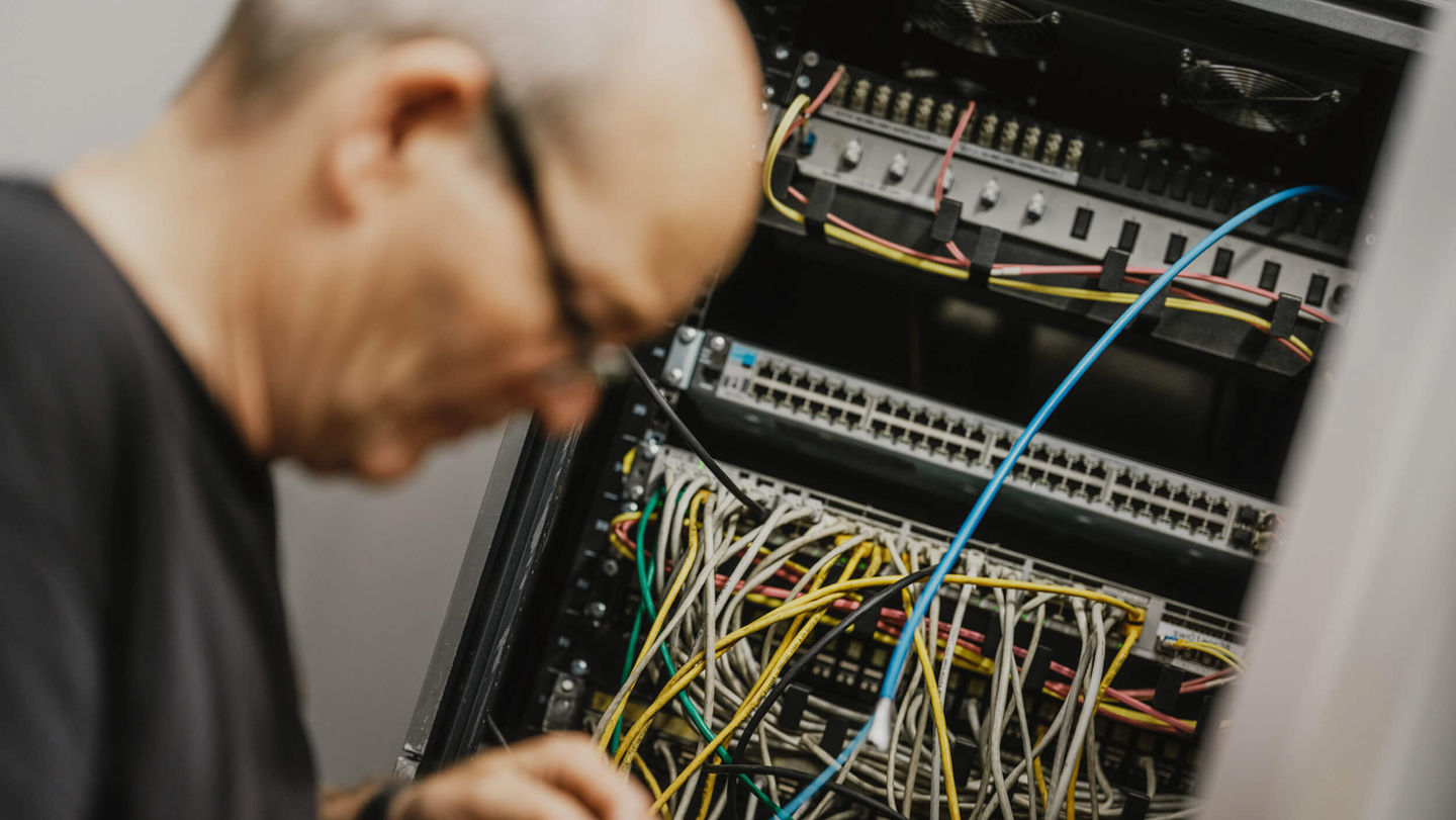 Elektriker arbeitet an einem Schaltschrank und verdrahtet einen Glasfaserkabel.