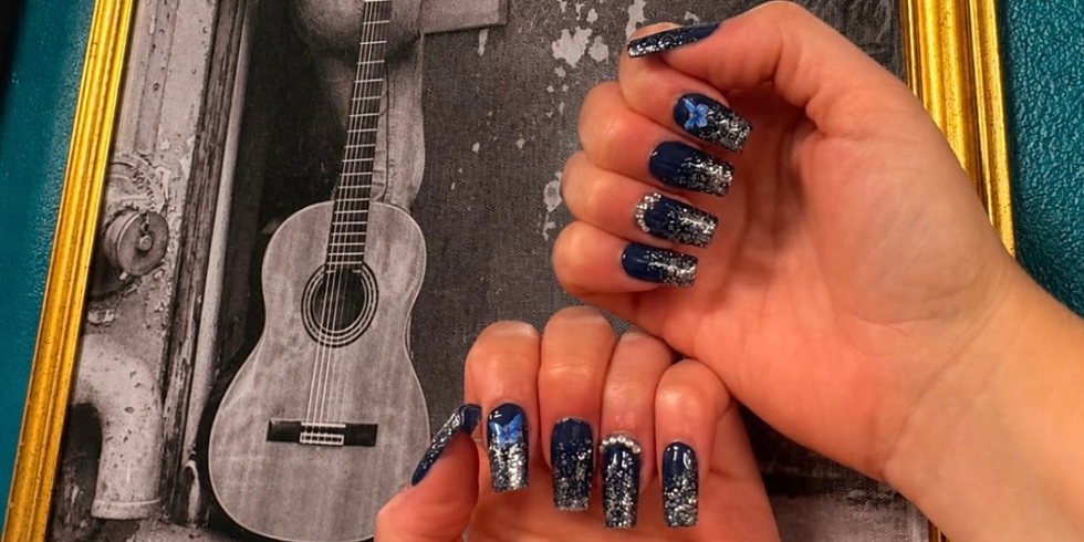 Hands with navy blue glitter nail art held over a framed black-and-white guitar photo.