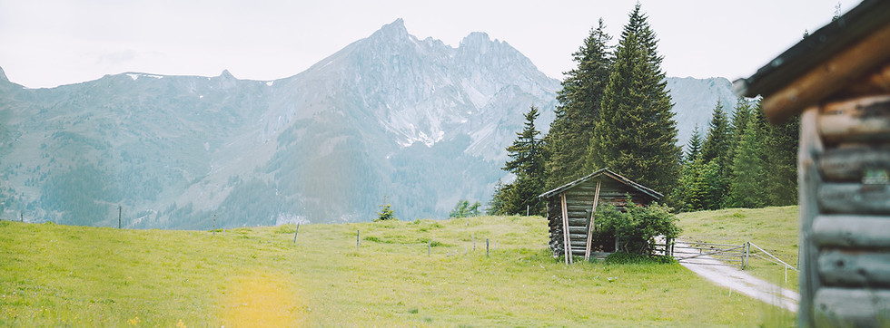Almhütte auf einer grünen Bergwiese vor Alpengipfeln.