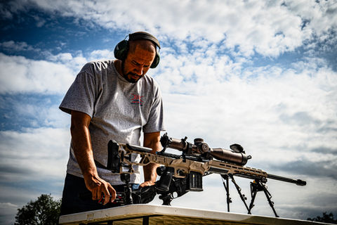 Man with ear protection adjusting a large rifle on a table