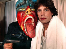 Color photograph of young Mick Jagger with a character in a red and blue mask