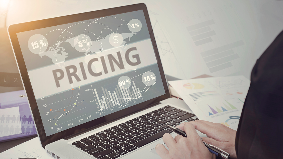 Laptop screen shows PRICING with sales charts and percentages while a person holds a pen at a desk with reports.