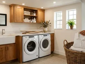 Shaker style plywood cabinets with shaker drawer fronts, quartz countertop, front load washer and dryer in a Florida garage laundry room, warm natural lighting, partial hand folding white garment into wicker basket