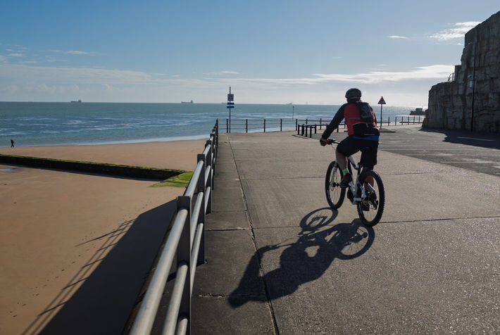 As a cyclist rides along the Margate seafront, a single figure walks along the distant shoreline.