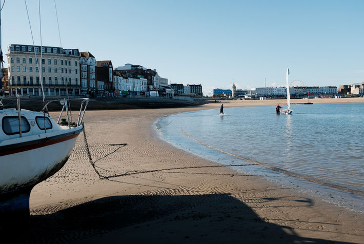 Margate beach at low tide, an owner walking through the water to his boat.