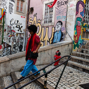 The walls of this street in Lisbon, Portugal have been decorated with colourful street art. The stylishly dressed lady is walking down the steps on her way to work.