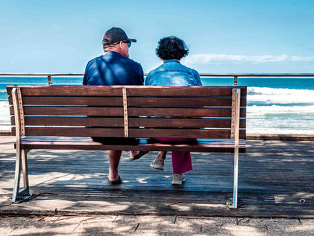 An elderly couple sitting together on a bench at Dee Why Beach in Sydney, looking out over the ocean.