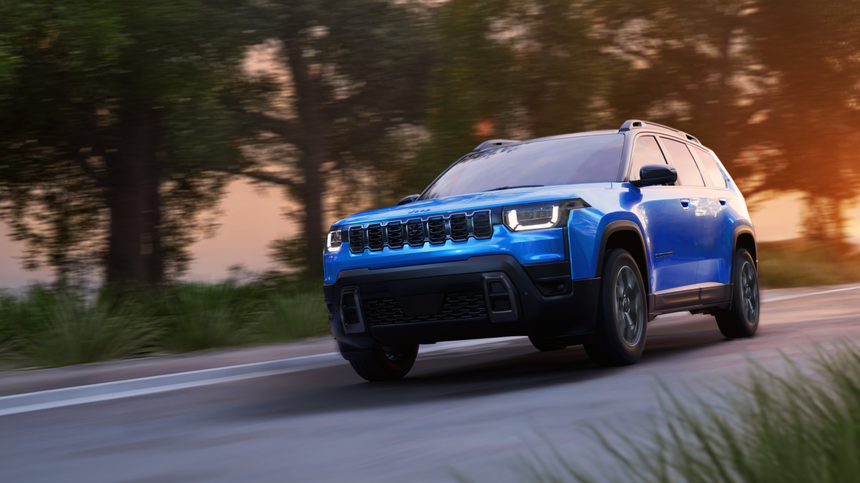 Blue Jeep Cherokee driving on a road at sunset