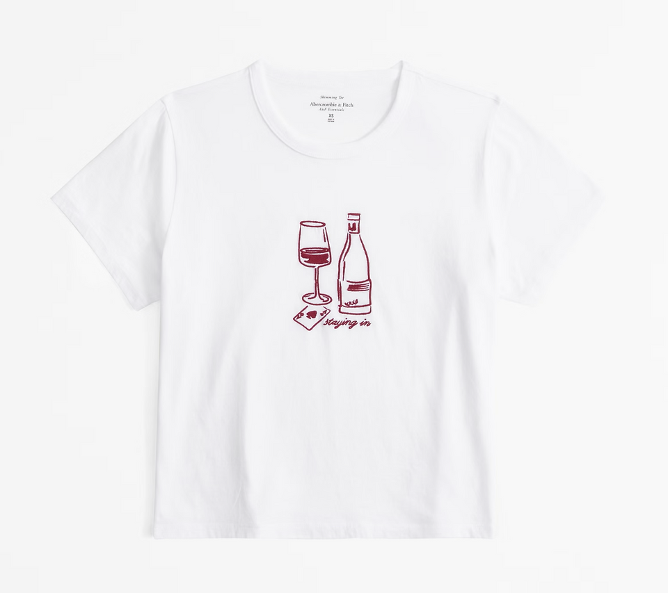 A white t-shirt with burgundy embroidery showing a red wine glass with wine in it and a bottle of wine
