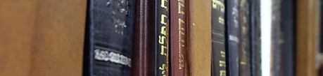 A close-up view of the spines of Hebrew prayer books on a library shelf.