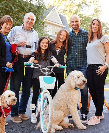 Three generations of a family, who benefit from insurance protection, standing together with two large dogs outside in front of a house