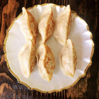Six golden brown pan-fried dumplings on a white plate.