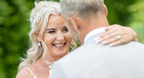 bride and groom portrait, bride smiles whilst holding her hand around grooms face. 