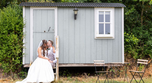 Bride and groom portrait sat kissing on each ither on the steps of a little cabin at the river lands, flax fleet.