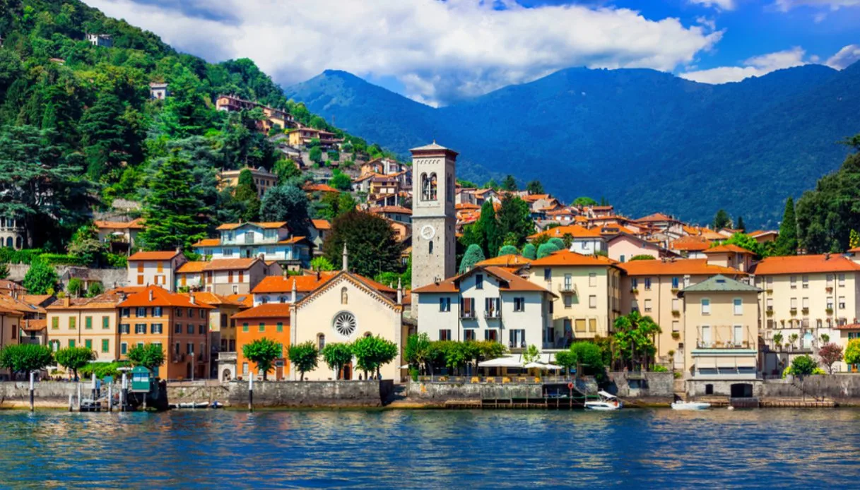 Vista del paese con chiesa e campanile dal lago blu. sullo sfondo montagna con alberi verdi