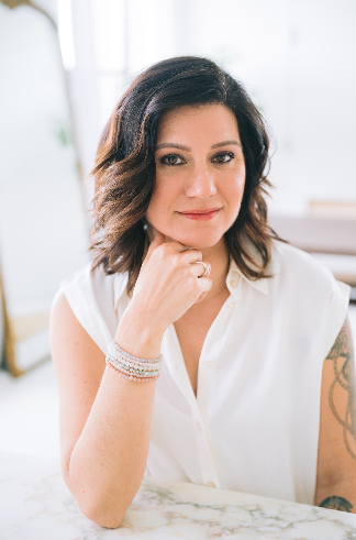 Woman in white blouse, seated at marble table, rests her chin on her hand. Soft light, calm expression, with blurred background.