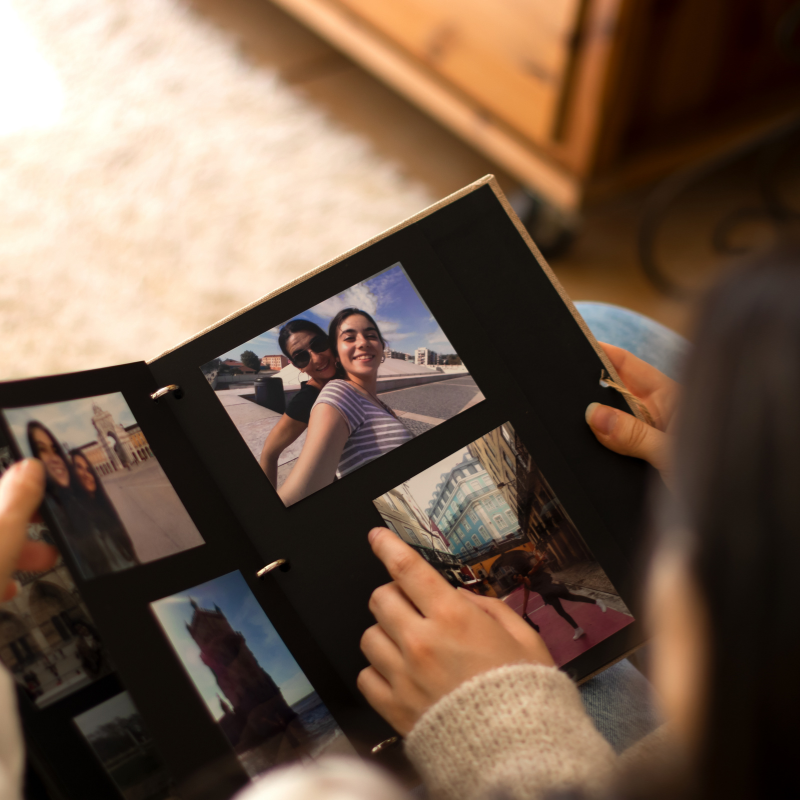 Hands hold a photo album with travel photos. Cozy indoor setting with a warm wooden background. Focus on images, bright and vivid.