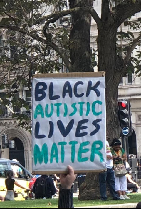 White placard with Black and Green text: It reads. Black Autistic Lives Matter 