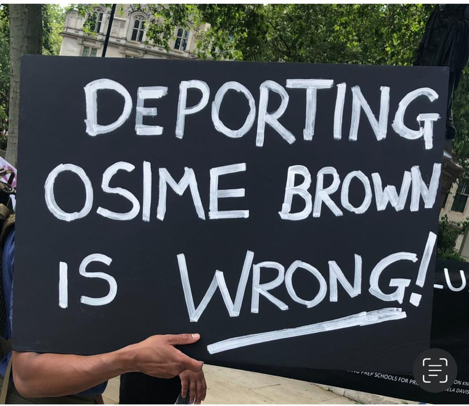 Black placard with white text. It reads in capitals: Deporting Osime Brown is Wrong