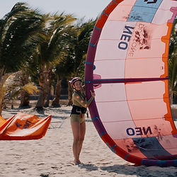 A student holds a red kite in her hands at Ponta Preta Beach, ready to launch it