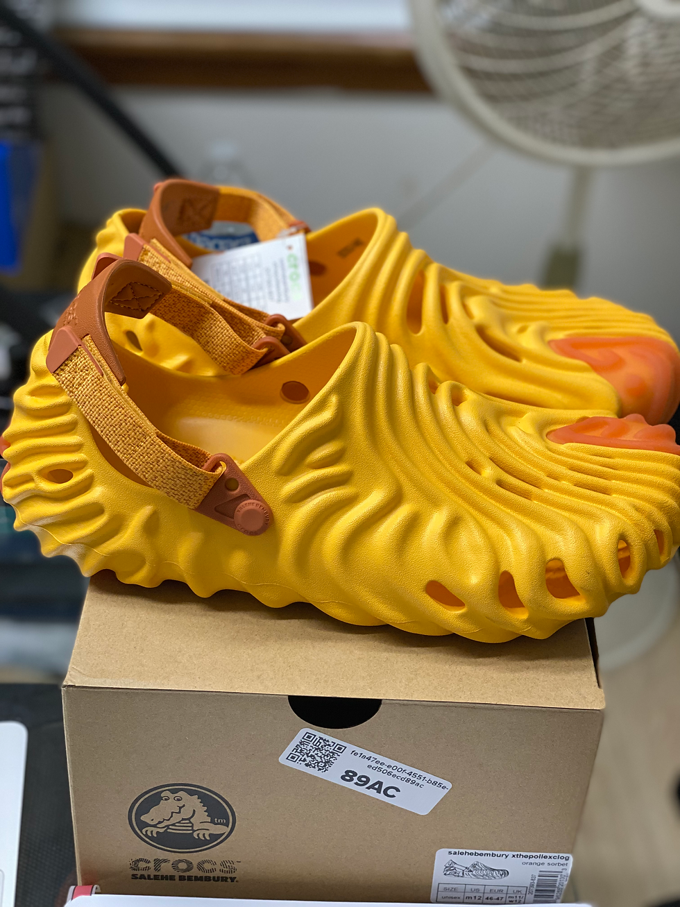 Pair of bright yellow and orange Salehe Bembury Crocs "89AC" on box.