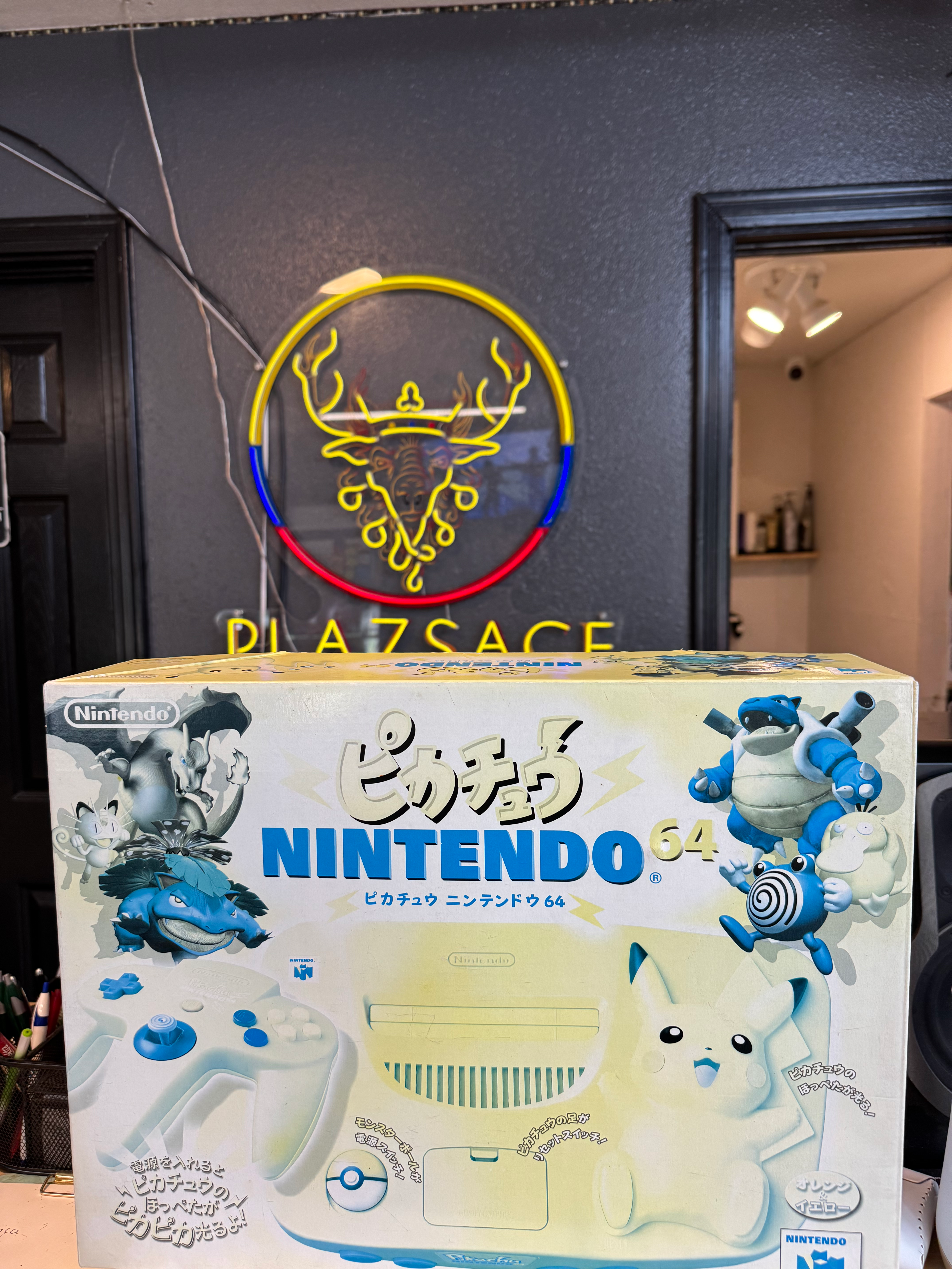 PLAZSAGE neon sign above a Pikachu Nintendo 64 console box.
