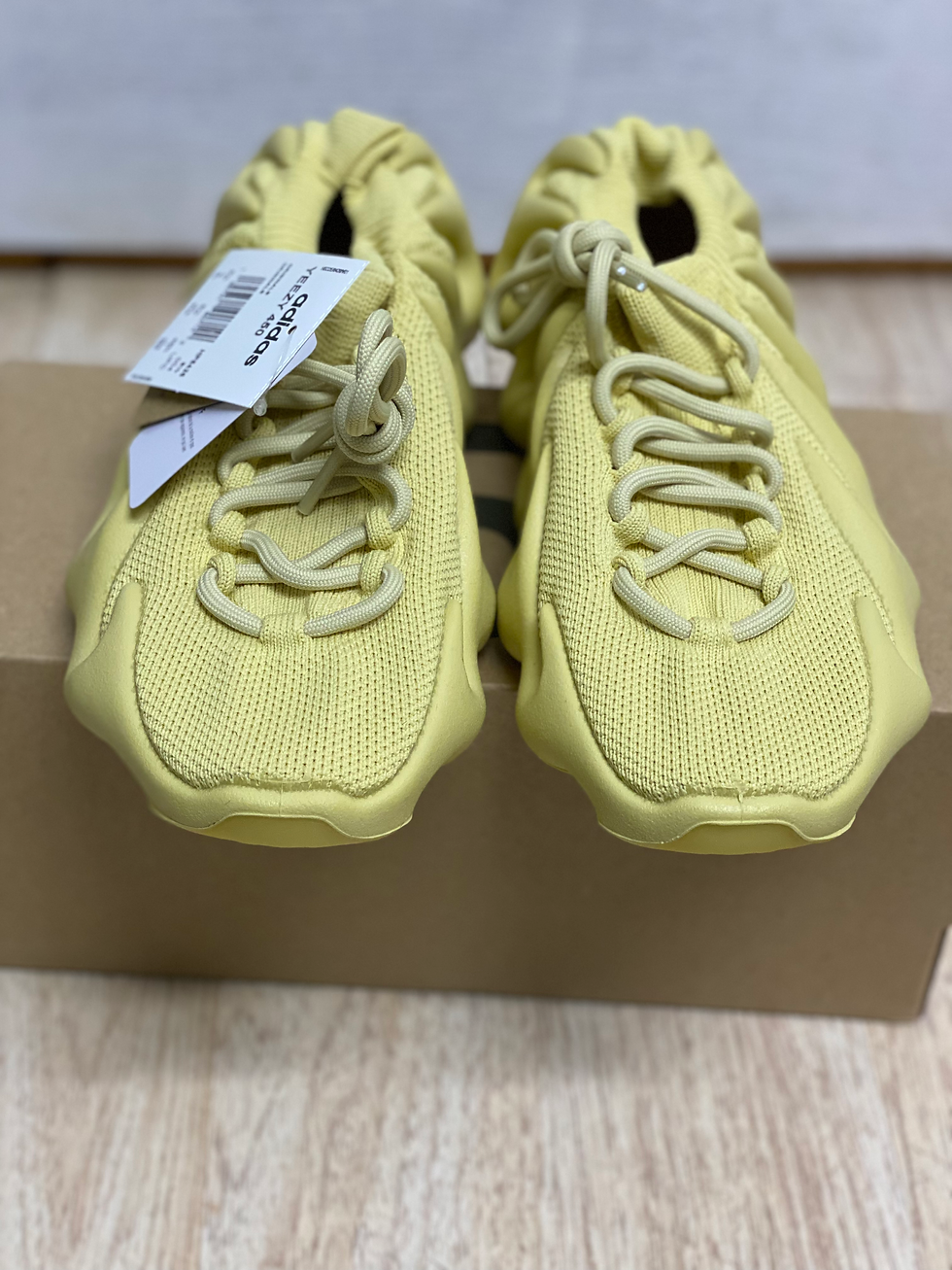Pair of light yellow Yeezy sneakers with tag on brown box.