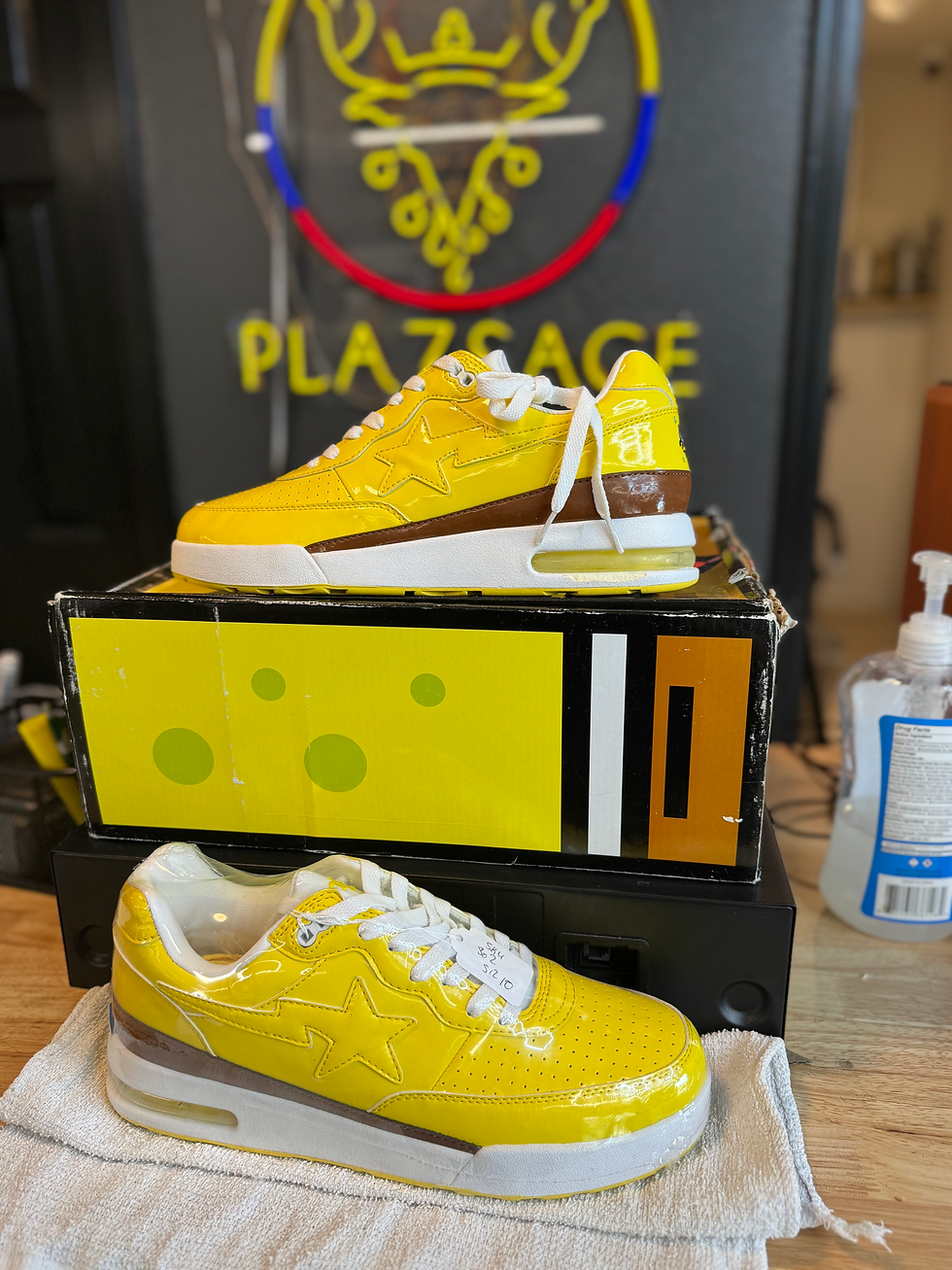 Yellow BAPE STA SpongeBob sneakers displayed on box, PLAZSAGE sign background.