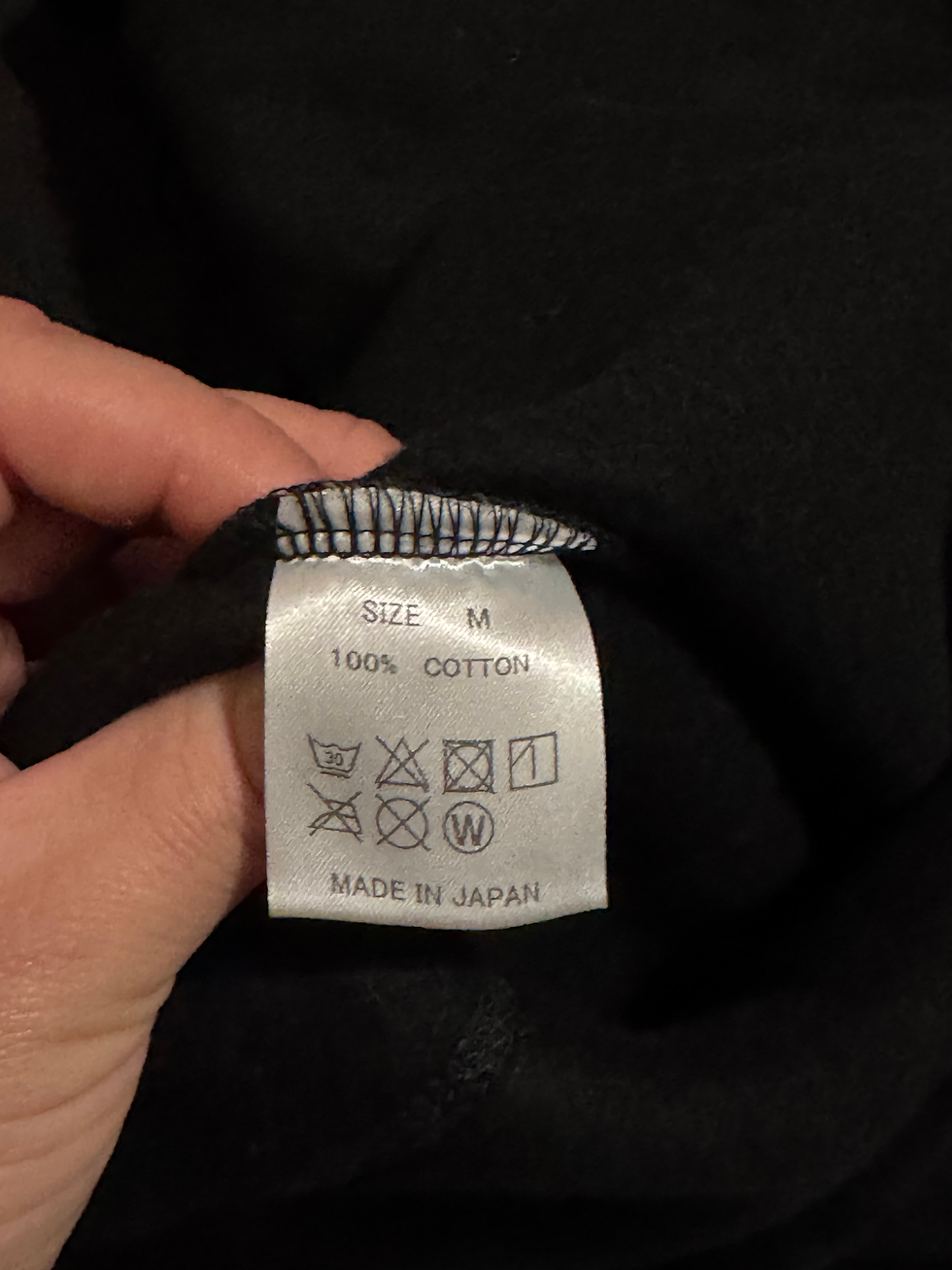 Miniatura: Hand holding clothing label: SIZE M, 100% COTTON, MADE IN JAPAN.